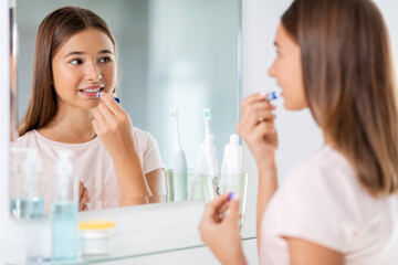 Obraz na płótnie Canvas beauty and cosmetics concept - teenage girl applying lip balm and looking to mirror at home bathroom