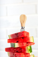Fresh red watermelon slices with a knife on wooden board on vertical white background. Raw berry with black seeds for summer vegan dessert.