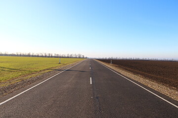 Asphalt road near agricultural fields and blue sky on a backround