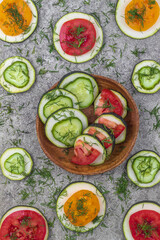 In the center, in a wooden plate, raw zucchini sandwiches with cucumbers and tomatoes