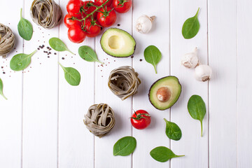 Cooking pasta with spinach nests, cherry tomatoes and avocados on a white wooden background. Flat lay style