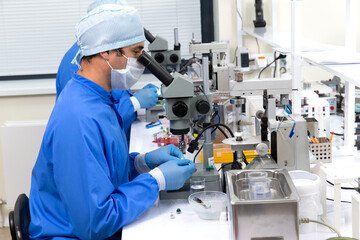 Fototapeta na wymiar A male scientist in a mask looks through a microscope in a laboratory.