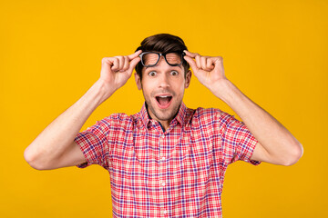 Portrait of attractive amazed cheerful guy geek wearing touching specs news reaction isolated over vibrant yellow color background