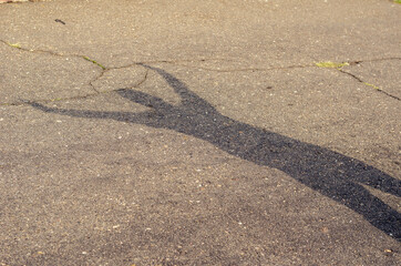 Fototapeta na wymiar A shadow with his hands in the air on the asphalt. A female silhouette on a cracked road. Daytime. Selective focus.