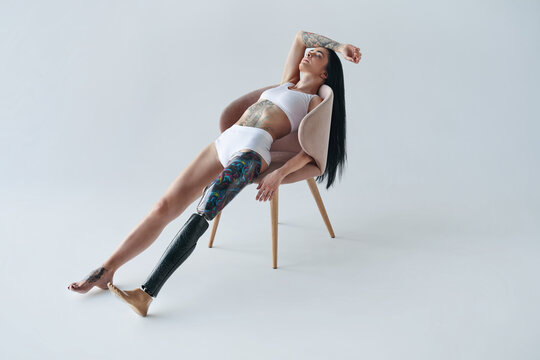 Tattooed girl with prothesis leg laying at the chair at the studio