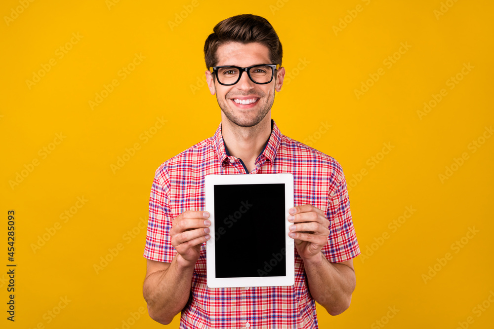 Poster portrait of attractive cheerful guy holding in hands tablet copy space isolated over bright yellow c