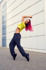girl in full-length sportswear rose on her toes, dances and trains against background of building