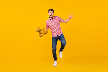 Fototapeta na wymiar Full length photo of cheerful young positive happy man hold teddy bear smile walk isolated on yellow color background