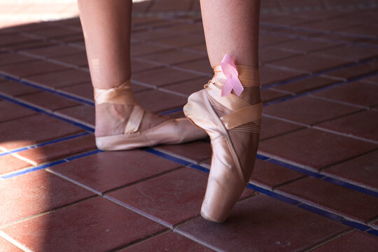 Classical ballet dancer's feet on points. On the bow of the shoes you can see a pink ribbon in solidarity with breast cancer. Breast cancer and classical ballet concept