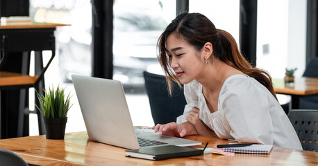 Fototapeta premium Smiling asian girl student using laptop computer study online with teacher, happy young woman learn language listen lecture watch webinar write notes look at laptop sit in cafe, distant education.