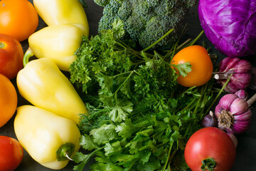 Green vegetables, broccoli, peppers, cabbage, tomatoes and garlic on a dark background, top view.
