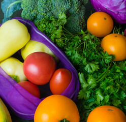 Lots of vegetables: squash, peppers, cilantro, parsley, cabbage, broccoli and tomatoes on a dark tabletop. Vegetables in a reusable fruit and vegetable bag. Ecology protection concept