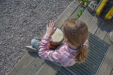 the girl child with a djembe drum outdoor on the porch of the house photo without processing