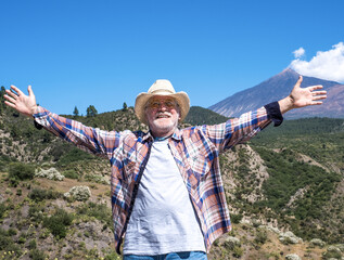 Happy senior man enjoying the nature in mountains with raised arms. Freedom concept
