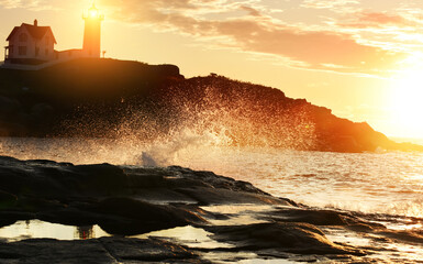 Dawn on the ocean. View of the lighthouse on the rock and splashing waves against the background of the rising sun. USA. maine. Cape Neddick Lighthouse (Nubble Light)