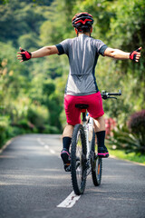 Woman no handed cycling on tropical park trail in summer