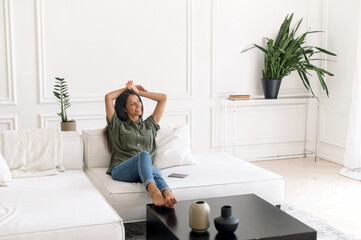 Harmony and balance concept. Carefree and serene indian woman resting on the comfortable couch at...