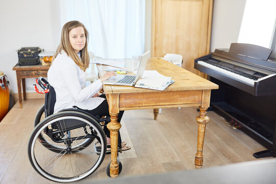 Frau mit Behinderung im Rollstuhl am Laptop im Wohnzimmer