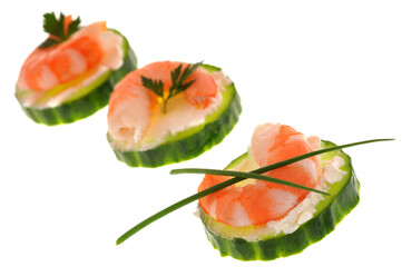 Amuse-bouches avec des rondelles de concombre, une crevette,  de la ciboulette et du persil en gros plan sur fond blanc