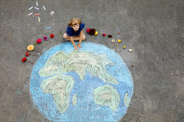Little preschool girl with flowers and earth globe painting with colorful chalks on ground....