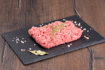 Ground beef with thyme and spices on a stone board over a wooden background.