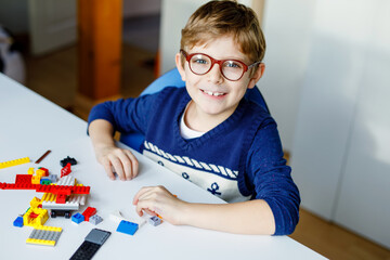 Little blond child with eye glasses playing with lots of colorful plastic blocks. Adorable school...