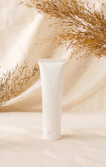 White plastic tube on linen drapery and dry branch of meadow plant. Concept eco organic cosmetic with natural extracts. Mock up skin care cosmetic product