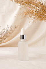 Serum bottle beauty product mockup on linen drapery and dry branch of meadow plant. Concept eco organic cosmetic with natural extracts. White frosted glass container mockup skincare cosmetic product