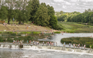 Lots of people swim and cross the Venta waterfall - the widest waterfall in Europe, Kuldiga, Latvia.