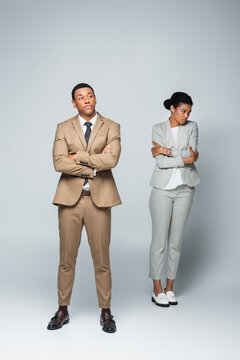 Full Length Of Arrogant Businessman With Crossed Arms Near Upset African American Woman On Grey