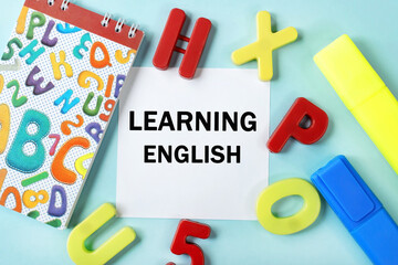 learning English is written on a white sheet of paper that lies on a blue background near a notebook and plastic multi-colored letters. Educational concept