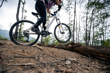 Fototapeta na wymiar Woman jumping over a log cycling on mountain top forest trail