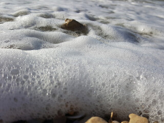 Sea foam surf and shiny multi-colored pebbles. The sea wave has foamed and covers the pebble beach. pebble stones on the sea beach, the rolling waves of the sea with foam