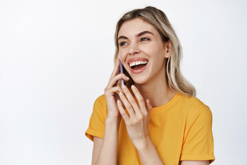 Fototapeta premium Close up of happy woman talking on mobile phone, laughing on call, standing against white background in yellow t-shirt