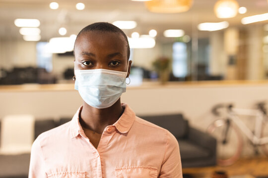 Portrait of african american female creative wearing face mask at work, looking to camera