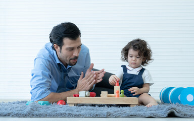 Caucasian young father clapping hands to admire his little kid sitting on floor playing wooden blocks toys together at home. Dad with beard in shirt and tie spends time with his child after work