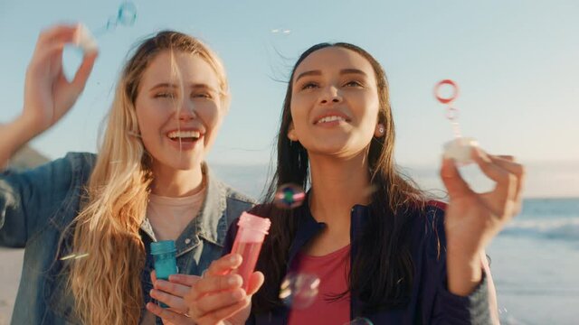 teenage girls blowing bubbles on beach at sunset best friends having fun summer playing by the sea enjoying friendship