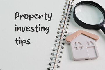 Magnifying glass, toy house and notebook with text PROPERTY INVESTING TIPS