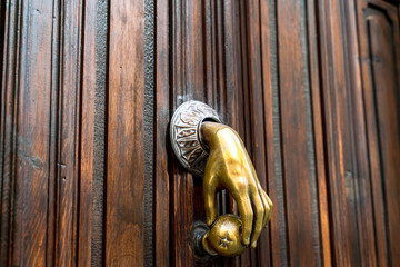 beautiful door knocker in the shape of a golden hand made of bronze installed on a wooden door..