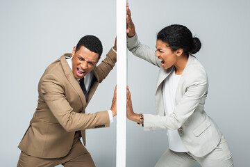angry african american businessman and businesswoman pulling wall and screaming on grey, gender...