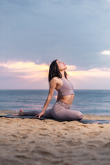 Fototapeta na wymiar Young Woman doing yoga at the beach at sunrise. Healthy and active lifestyle.