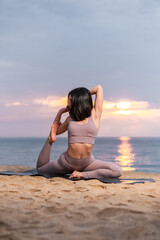 Fototapeta na wymiar Young Woman doing yoga at the beach at sunrise. Healthy and active lifestyle.