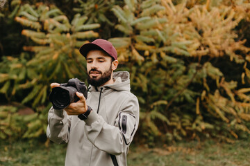 stylish bearded photographer with a camera in his hands takes a photo in the autumn park