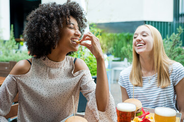 two young women having fun while eating snacks at restaurant, group of multiethnic people tasting junk food, diversity and inclusion concept of multicultural lifestyle