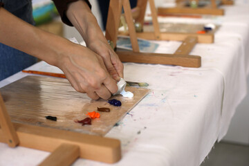 Female hands squeeze white oil paint on a wooden palette. Preparations for art workshop