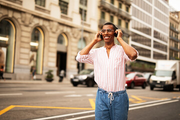Fototapeta premium Cheerful guy with the headphones. Young african man listening the music outdoors