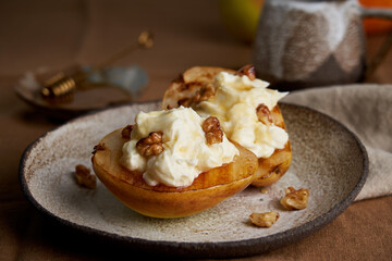 Side view of sweet grilled pears with cream and nuts. Hot coffee and honey on wooden table. Horizontal of rustic delicious dessert. Autumn meal. Sliced fruit