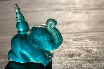 Beautiful backlit translucent blue crystal buddhist statue of kneeling elephant carrying stupa on bright wooden background