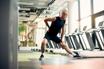 Mature athletic man stretches while warming up for sports training in gym.