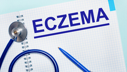 On a light blue background, an open notebook with the word ECZEMA, a blue pen and a stethoscope. View from above. Medical concept